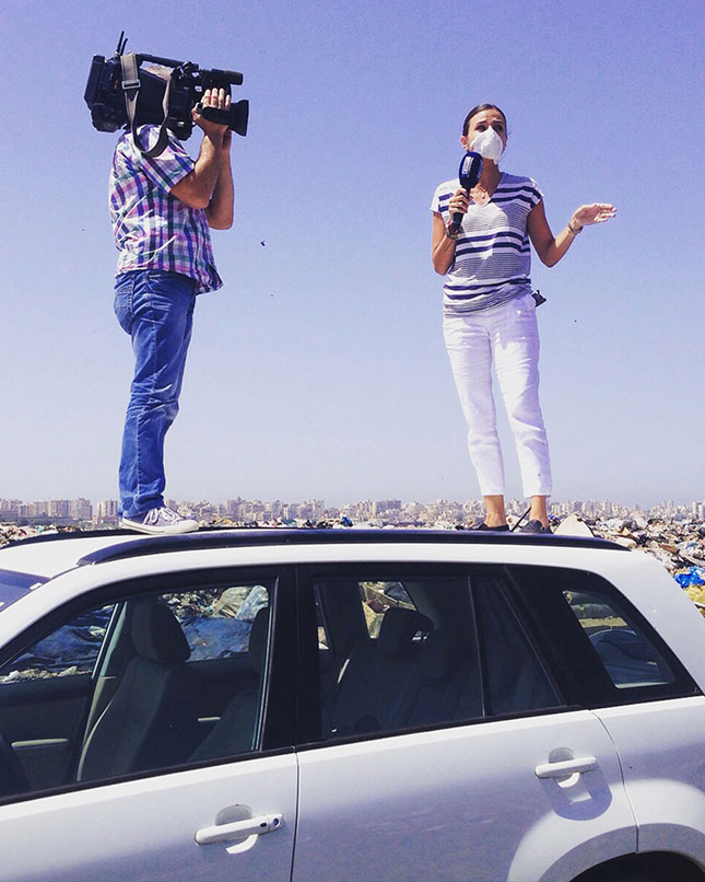 Dalal Mawad, masque sur le visage et micro à la main, couvrant la crise des déchets au Liban depuis le toit d'une voiture devant une décharge